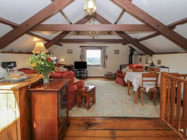 A living room with wooden beams dining table and red sofas at Beckaford Cottage in Bovey Tracey
