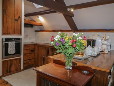 A kitchen with wooden cabinets, an oven, a vase of flowers on a wooden counter, and tea set at Beckaford Cottage in Bovey Tracey