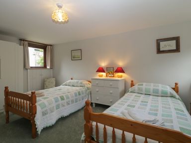 A bedroom with two single wooden beds with patterned bedspreads and a white dresser with two lamps at Beckaford Cottage in Bovey Tracey