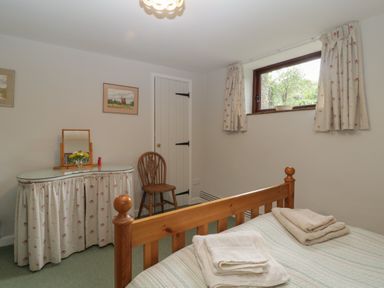 A bedroom with a wooden bed and folded towels a vanity with a mirror and chair and a small window with curtains at Beckaford Cottage in Bovey Tracey