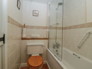 A bathroom with a toilet and a bathtub with a glass shower screen at Beckaford Cottage in Bovey Tracey