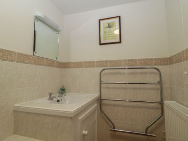 A bathroom sink with a mirror above and a metal towel rack next to a radiator at Beckaford Cottage in Bovey Tracey