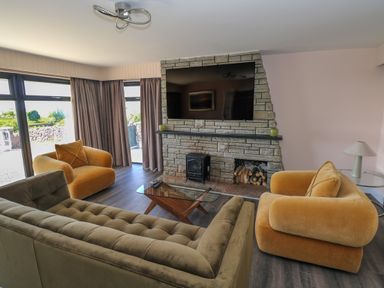 A living room with armchairs and sofa facing a stone fireplace with a mounted television at Cushranny in Mulranny County Mayo