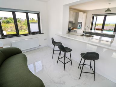An open kitchen and dining area with three black bar stools a green couch and large windows at Cushranny in Mulranny County Mayo