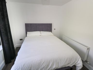 A bedroom with a bed with white bedding a gray headboard a radiator on the wall and black curtains at Cushranny in Mulranny County Mayo