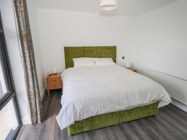 A bedroom with a bed with white bedding green headboard two bedside tables and a window with curtains at Cushranny Mulranny County Mayo