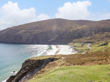 A coastal landscape with a sandy beach, a rocky hillside, and a winding road near Cushranny in Mulranny County Mayo
