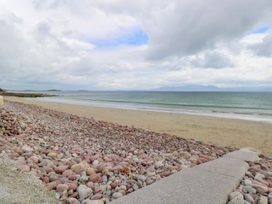 A rocky shoreline with a sandy beach and calm sea under a cloudy sky