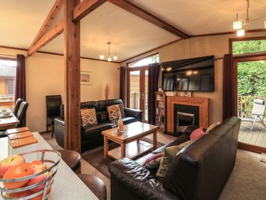 A living room with black leather sofas a wooden coffee table a TV mounted above a fireplace and a fruit basket on a counter at Templar Rise 16 - Devon Comfort Finlakes Holiday Park near Chudleigh