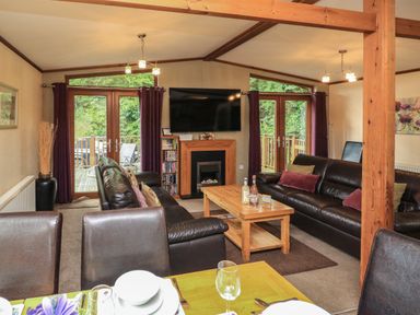 A living room with two dark leather sofas a wooden coffee table wall-mounted television and glass doors at Templar Rise 16 - Devon Comfort in Finlakes Holiday Park near Chudleigh