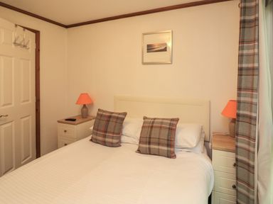 A bedroom with a double bed two plaid cushions two bedside tables with lamps and plaid curtains at Templar Rise 16 - Devon Comfort in Finlakes Holiday Park near Chudleigh