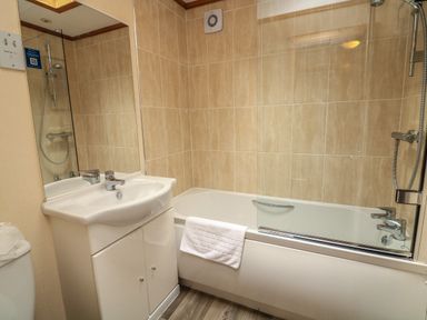A bathroom with a sink and cabinet next to a bathtub with a shower and a partial glass screen at Templar Rise 16 - Devon Comfort Finlakes Holiday Park near Chudleigh