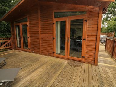 A wooden deck with lounge chairs and double glass doors leading into a wooden cabin at Templar Rise 16 - Devon Comfort Finlakes Holiday Park near Chudleigh