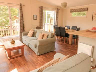 A living room with green sofas a wooden coffee table and a dining area with black chairs at Deer Park 9 - Copse Corner Finlakes Holiday Park near Chudleigh