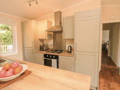 A kitchen with wooden countertops white cabinets a gas stove a toaster a kettle and a bowl of apples and tomatoes on the counter at Deer Park 9 - Copse Corner Finlakes Holiday Park near Chudleigh