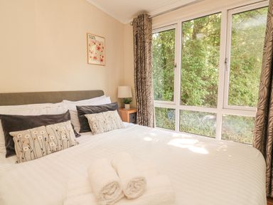 A bedroom with a large bed white linens rolled towels bedside table lamp and large window with patterned curtains at Deer Park 9 - Copse Corner in Finlakes Holiday Park near Chudleigh