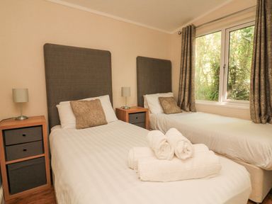 A bedroom with two single beds pillows bedside tables lamps and a window with curtains at Deer Park 9 - Copse Corner Finlakes Holiday Park near Chudleigh