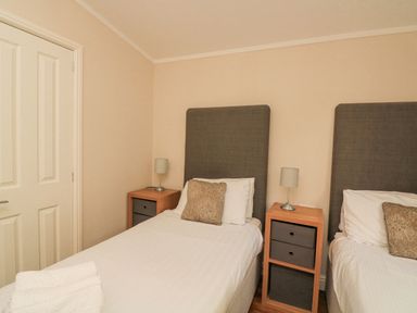 A bedroom with two single beds bedside tables with lamps and a door at Deer Park 9 - Copse Corner in Finlakes Holiday Park near Chudleigh