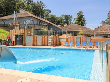 An outdoor swimming pool with a slide and blue lounge chairs next to a building at Deer Park 9 - Copse Corner Finlakes Holiday Park near Chudleigh