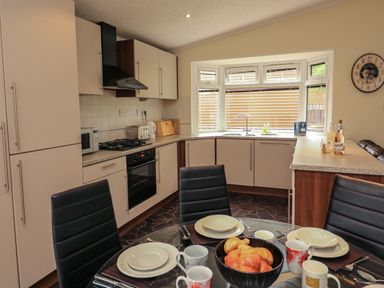 A kitchen with dining table set with cups plates and bread near a window at The Brambles 17 - Conkers Lodge Finlakes Holiday Park near Chudleigh