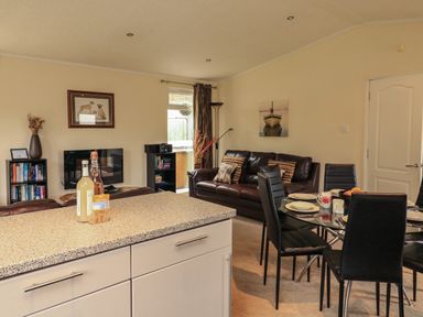 A living room with a brown leather sofa a glass dining table with black chairs and a kitchen counter at The Brambles 17 - Conkers Lodge Finlakes Holiday Park near Chudleigh