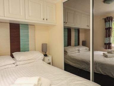 A bedroom with double bed white bedding bedside table and cabinet above at The Brambles 17 - Conkers Lodge Finlakes Holiday Park near Chudleigh