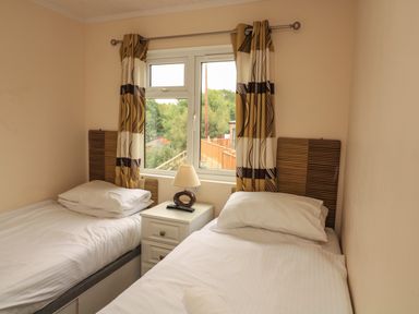 A bedroom with two single beds a bedside table and a window with curtains at The Brambles 17 - Conkers Lodge Finlakes Holiday Park near Chudleigh