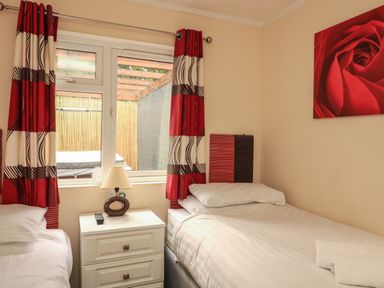A bedroom with two single beds a white bedside table with a lamp and remote and red curtains at The Brambles 17 - Conkers Lodge Finlakes Holiday Park near Chudleigh