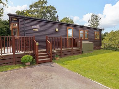 A wooden lodge with steps leading to a deck and grass lawn at The Brambles 17 - Conkers Lodge Finlakes Holiday Park near Chudleigh