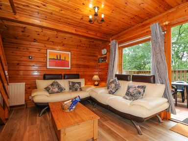 A living room with wooden walls and ceiling two cream sofas with pillows wooden coffee table and a window with curtains at Lodge 32 - Cowslip Finlakes Holiday Park near Chudleigh