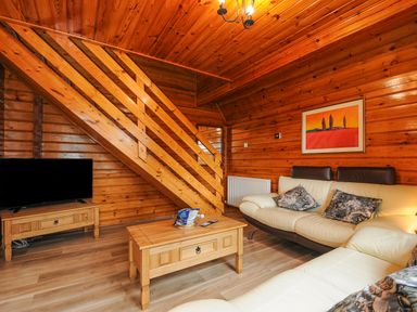 A wooden living room with stairs a television on a stand a coffee table and cream sofas with cushions at Lodge 32 - Cowslip Finlakes Holiday Park near Chudleigh