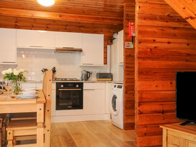 A kitchen with white cabinets a dining table with flowers and glassware and wooden walls at Lodge 32 - Cowslip Finlakes Holiday Park near Chudleigh