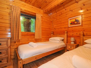 A bedroom with two single wooden beds white linens and a window with curtains at Lodge 32 - Cowslip in Finlakes Holiday Park near Chudleigh