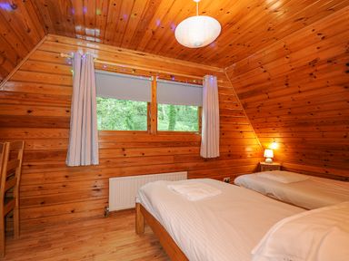 A bedroom with two single beds a wooden chair a window with curtains and a small lamp on a nightstand at Lodge 32 - Cowslip Finlakes Holiday Park near Chudleigh
