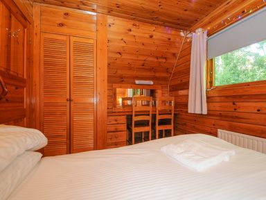 A bedroom with wooden walls a bed a desk with two chairs and a window at Lodge 32 - Cowslip in Finlakes Holiday Park near Chudleigh