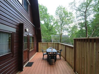 An outdoor wooden deck with a table and four chairs attached to a wooden cabin surrounded by trees at Lodge 32 - Cowslip Finlakes Holiday Park near Chudleigh