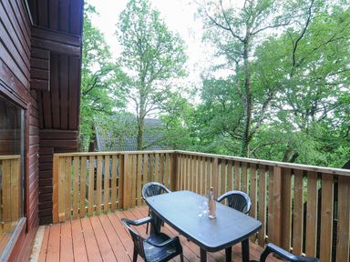 A wooden balcony with a plastic table and four chairs with trees in the background at Lodge 32 - Cowslip in Finlakes Holiday Park near Chudleigh