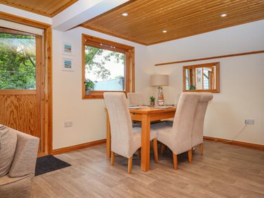 A dining area with a wooden table and four beige chairs near windows and a wooden door at Lodge 45 - Lazy Bear Finlakes Holiday Park near Chudleigh