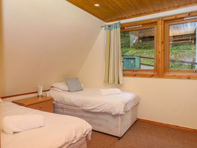 A bedroom with two single beds a wooden bedside table and a window with curtains at Lodge 45 - Lazy Bear in Finlakes Holiday Park near Chudleigh
