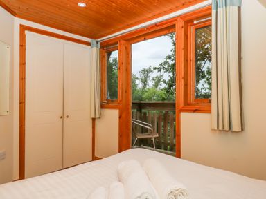 A bedroom with a bed and rolled towels near windows and a balcony with a chair at Lodge 45 - Lazy Bear in Finlakes Holiday Park near Chudleigh