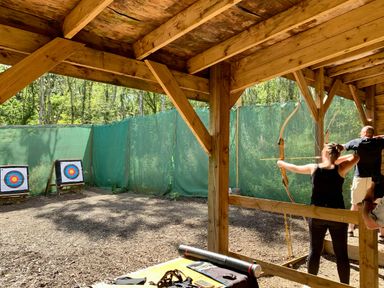 An outdoor archery range with two people aiming bows at targets under a wooden shelter at Lodge 45 - Lazy Bear Finlakes Holiday Park near Chudleigh