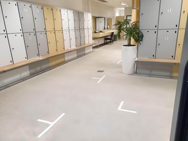 A changing room with lockers benches mirrors a potted plant and marked floor spaces