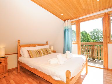 A bedroom with wooden bed and bedside tables with lights and an open door to a balcony at Lodge 47 - Primrose Lodge Finlakes Holiday Park near Chudleigh