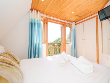 A bedroom with a bed with rolled towels and pillows near windows with blue curtains at Lodge 47 - Primrose Lodge in Finlakes Holiday Park near Chudleigh