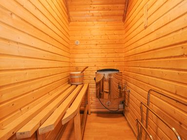 A wooden sauna room with a bench bucket and ladle heater and metal towel rack at Lodge 47 - Primrose Lodge in Finlakes Holiday Park near Chudleigh