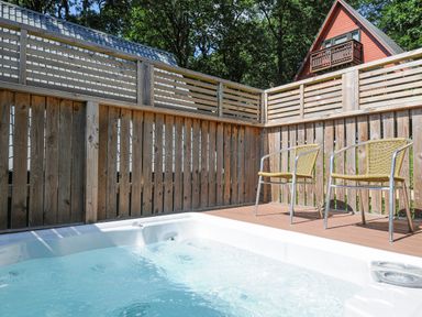 An outdoor hot tub with two chairs on a wooden deck and wooden fence surrounding it at Lodge 47 - Primrose Lodge in Finlakes Holiday Park near Chudleigh