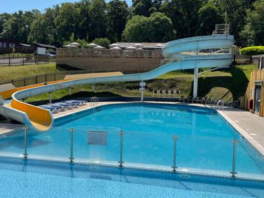 An outdoor swimming pool with a water slide surrounded by lounge chairs and a fenced area at Lodge 47 - Primrose Lodge Finlakes Holiday Park near Chudleigh