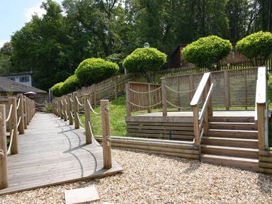 An outdoor area with wooden pathways, rope railings, trimmed bushes, and trees at Lodge 47 - Primrose Lodge Finlakes Holiday Park near Chudleigh