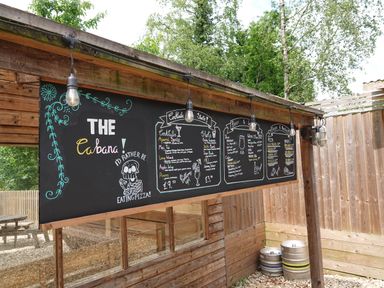 An outdoor wooden bar area with a large black chalkboard menu and hanging light bulbs