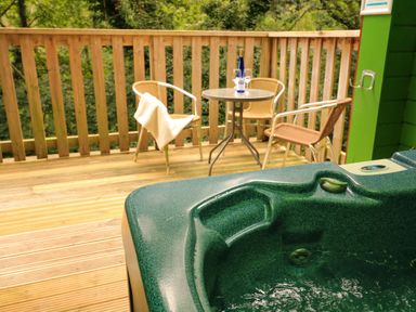 An outdoor deck with a hot tub a table with two chairs and a bottle with glasses at Lodge 58 - Oak Tree Lodge in Finlakes Holiday Park near Chudleigh